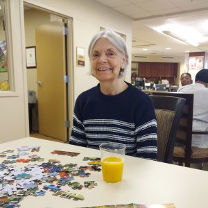 Woman smiling in the River Garden Adult Day Program with a puzzle in front of her