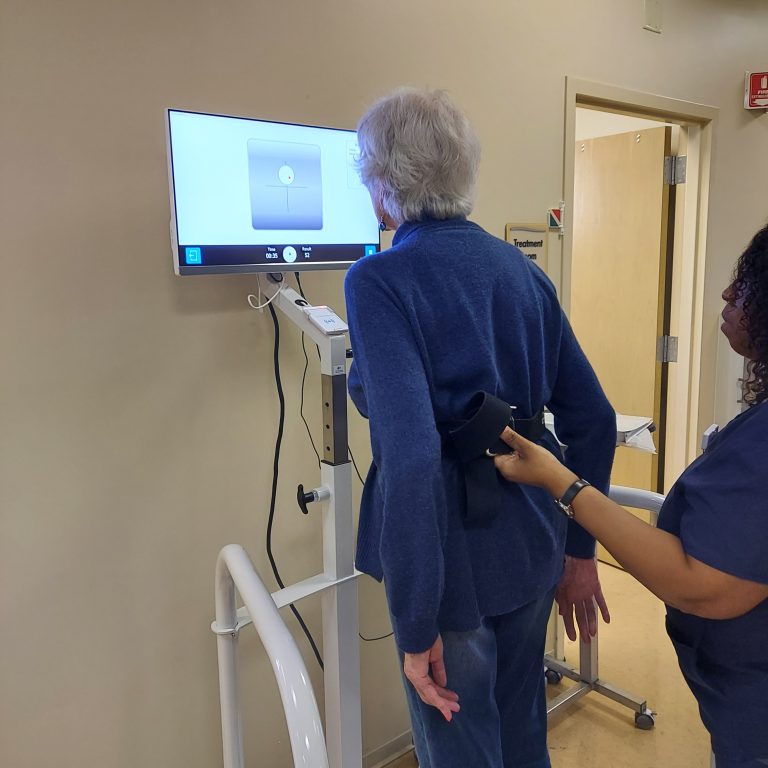 Elderly patient with therapist doing balance exercises in front of a screen displaying a target.