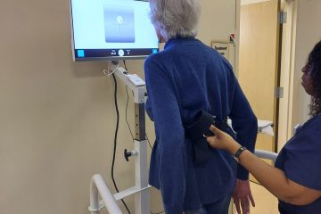 Elderly patient with therapist doing balance exercises in front of a screen displaying a target.
